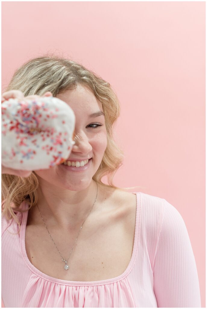 senior spokesmodel in light pink top holding sprinkled doughnut towards camera and smiling in millersville pennsylvania