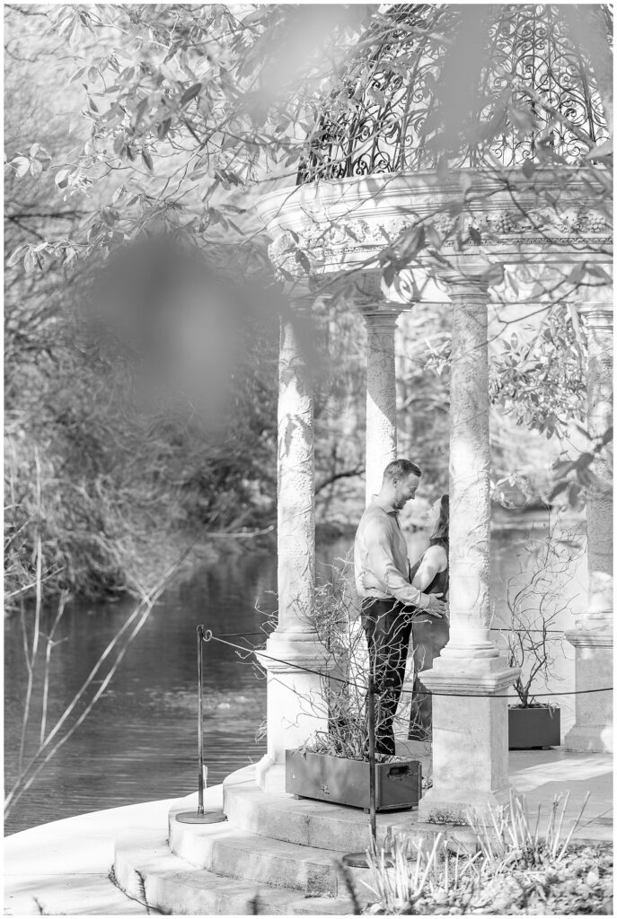 black and white photo of couple standing close beside white column at longwood gardens