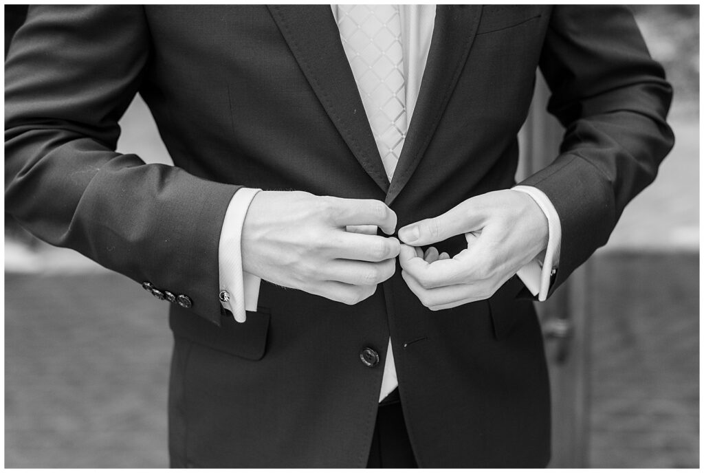 black and white photo of closeup photo of groom buttoning his black suit coat at the inn at leola village