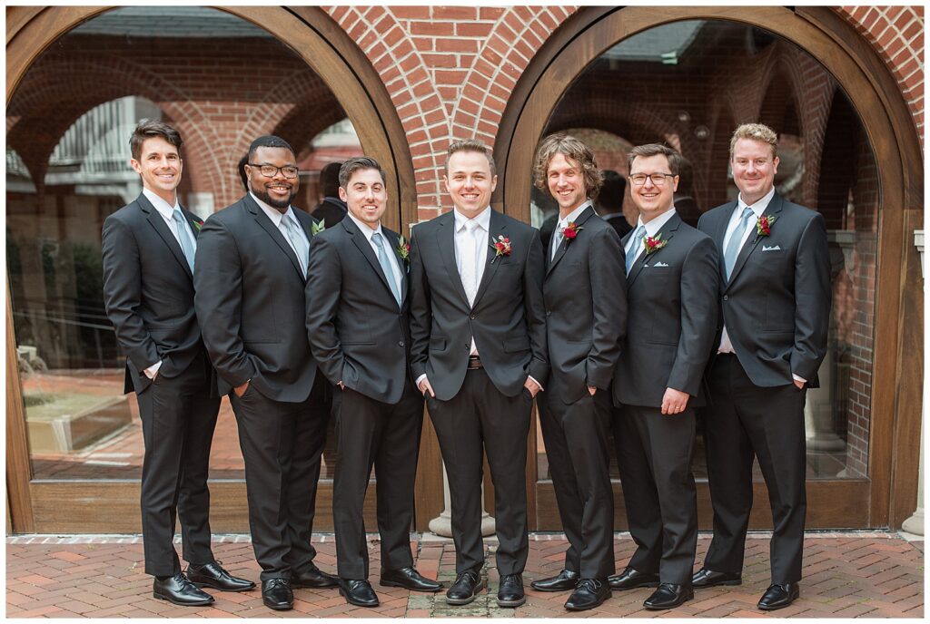 groom with his six groomsmen all in black suits by brick archway in lancaster county pennsylvania