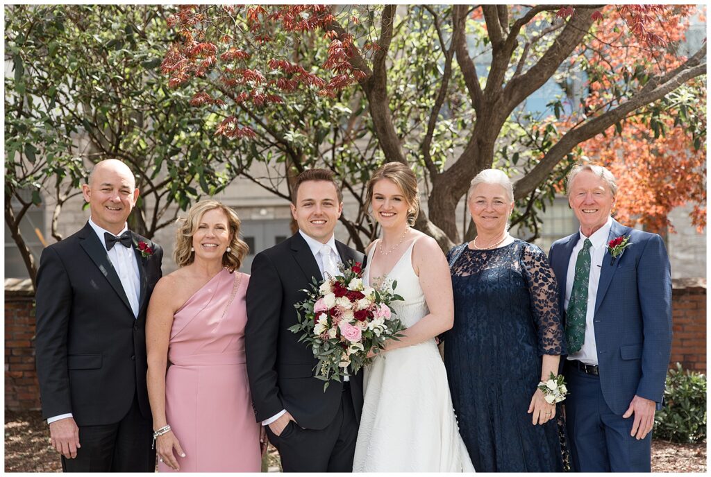 bride and groom with both sets of their parents all smiling at the camera by blooming tree in lancaster city