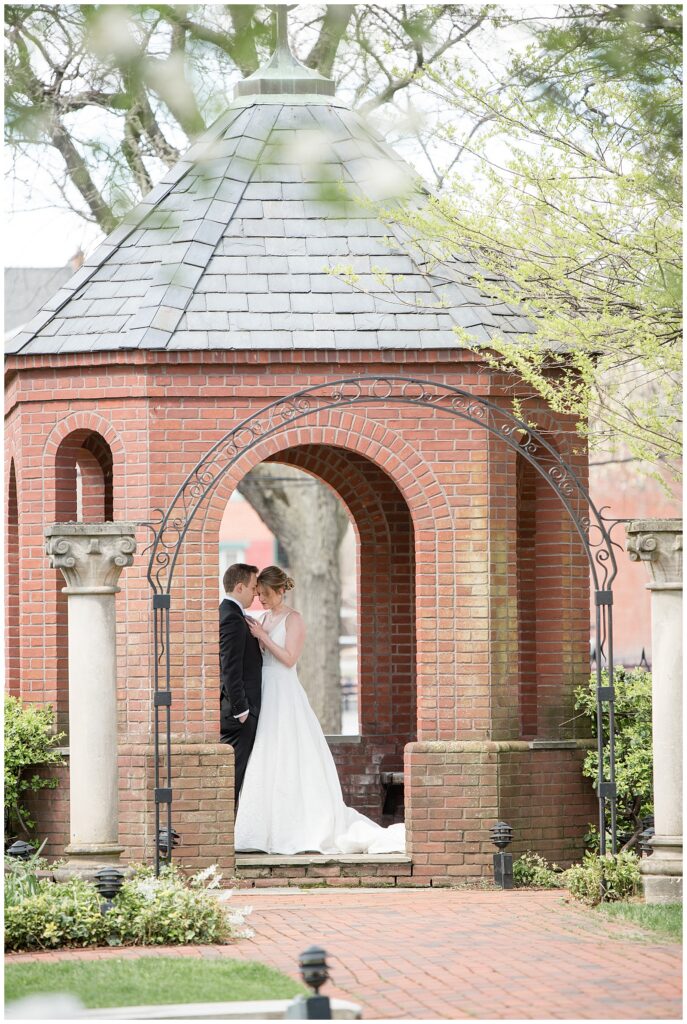 couple standing close together under brick gazebo at st. james episcopal church in lancaster pennsylvania