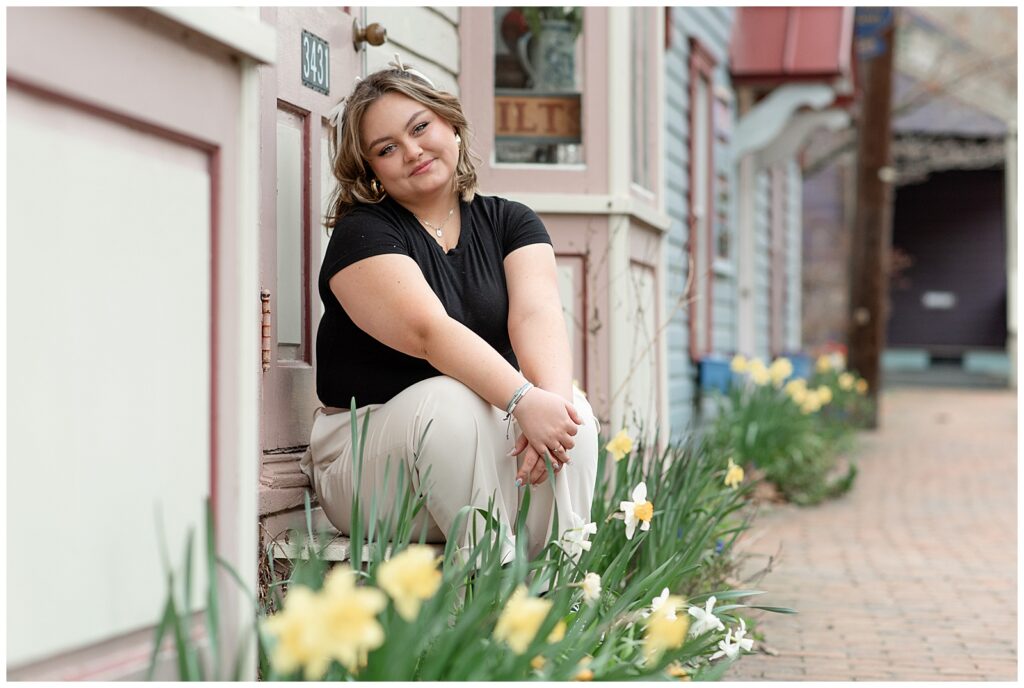 female senior spokesmodel sitting against building by daffodils at st. peter's village in chester county, pa