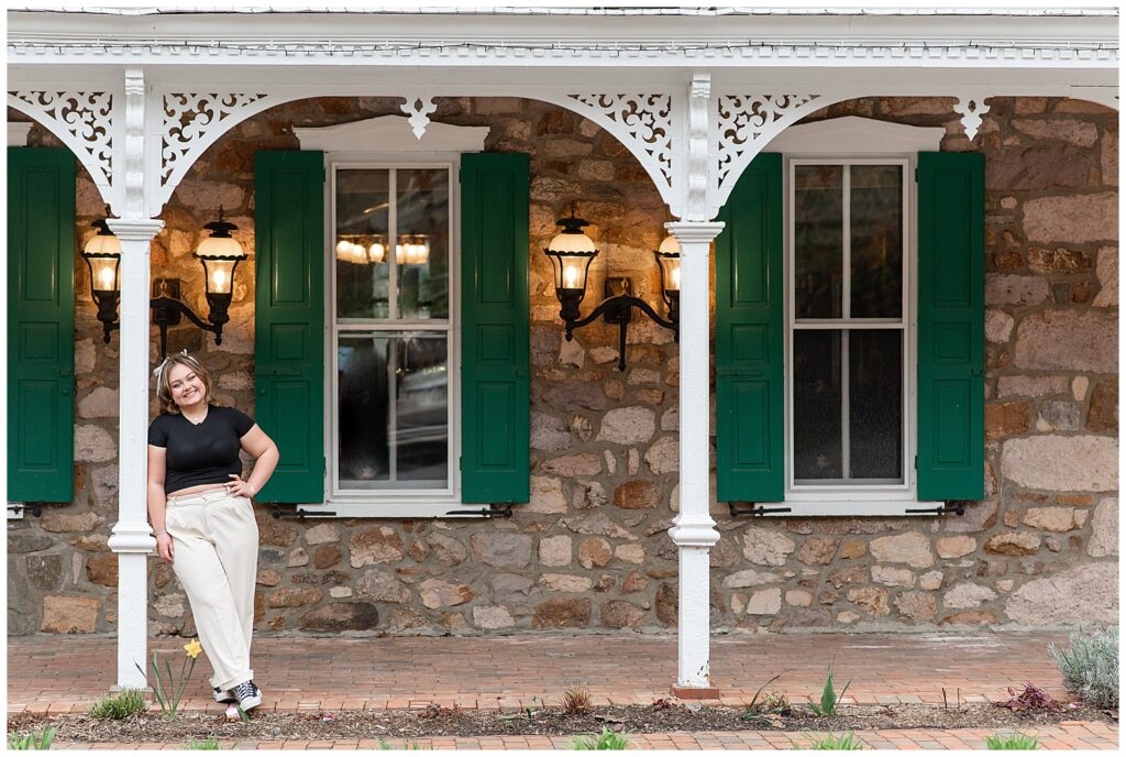 senior girl leaning against white porch column of old stone building at st. peter's village
