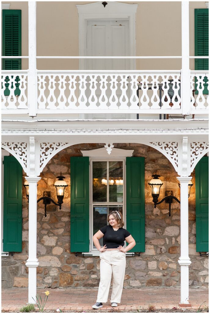 senior girl with hands on hips standing in between white porch columns at st. peter's village in pennsylvania