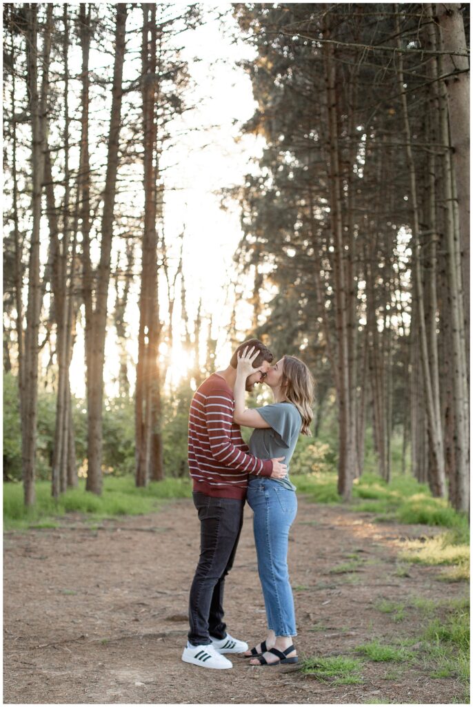 woman kissing man's forehead as they hug by rows of evergreen trees at sunset in lancaster pennsylvania