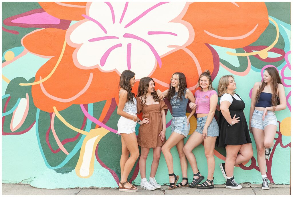 six senior girls in shorts and t-shirts of different colors by colorful flower mural in lancaster city