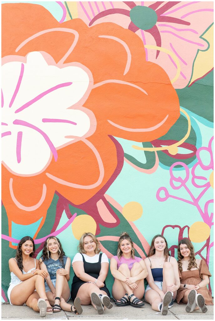 six senior girls sitting against flower mural with their legs extended toward the camera in downtown lancaster pennsylvania