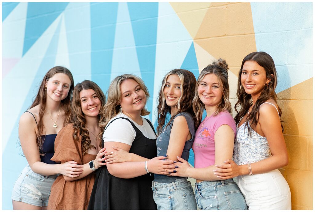 six senior girls huddled together with their arms around one another by painted mural wall in downtown lancaster pa