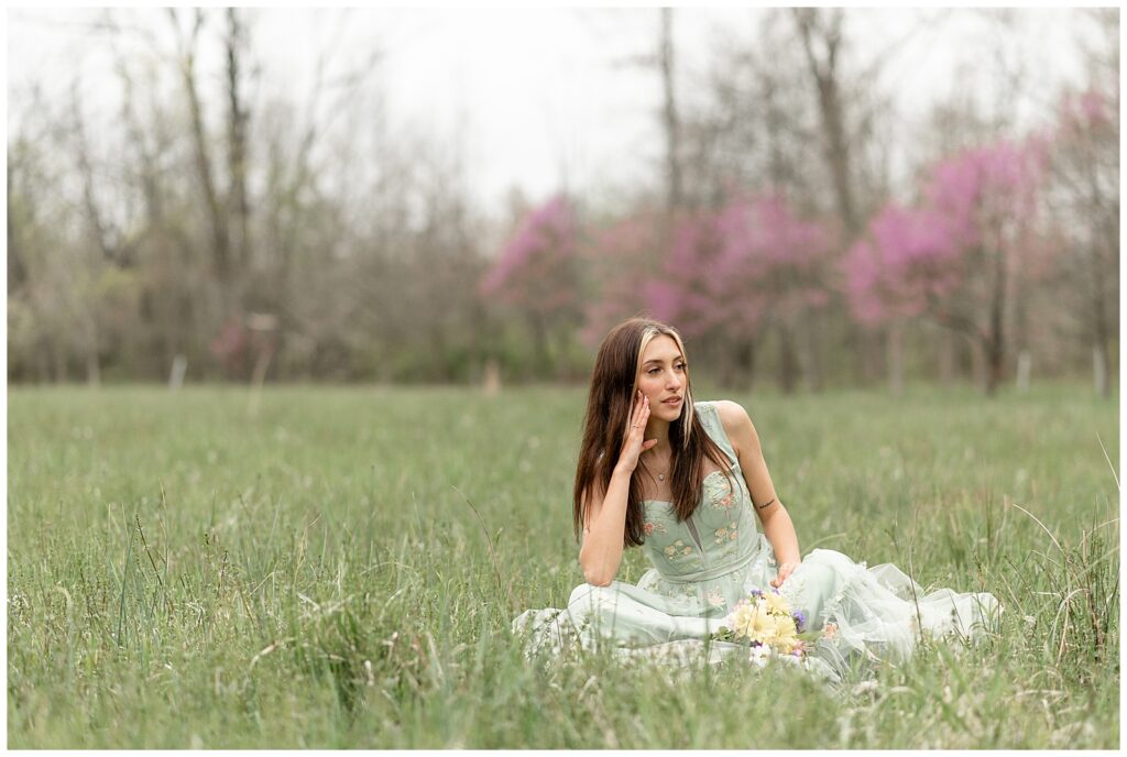senior spokesmodel sitting in middle of field with her right hand holding up her cheek as she looks left in lancaster county