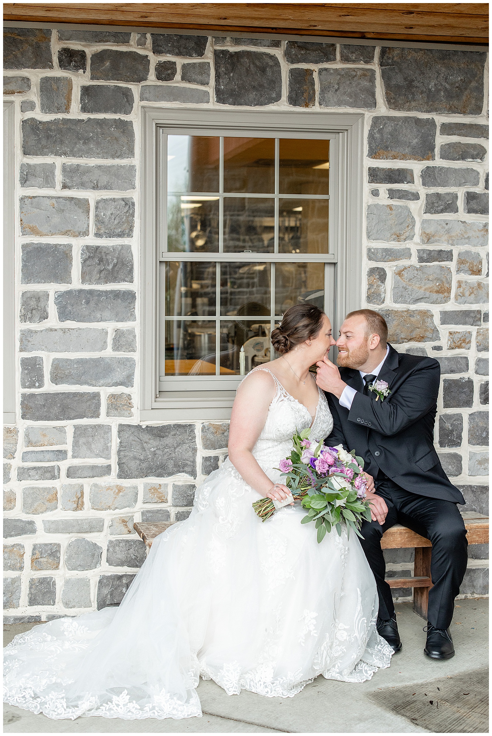 bride and groom on bench by stone wall almost kissing at brick gables in lancaster pa
