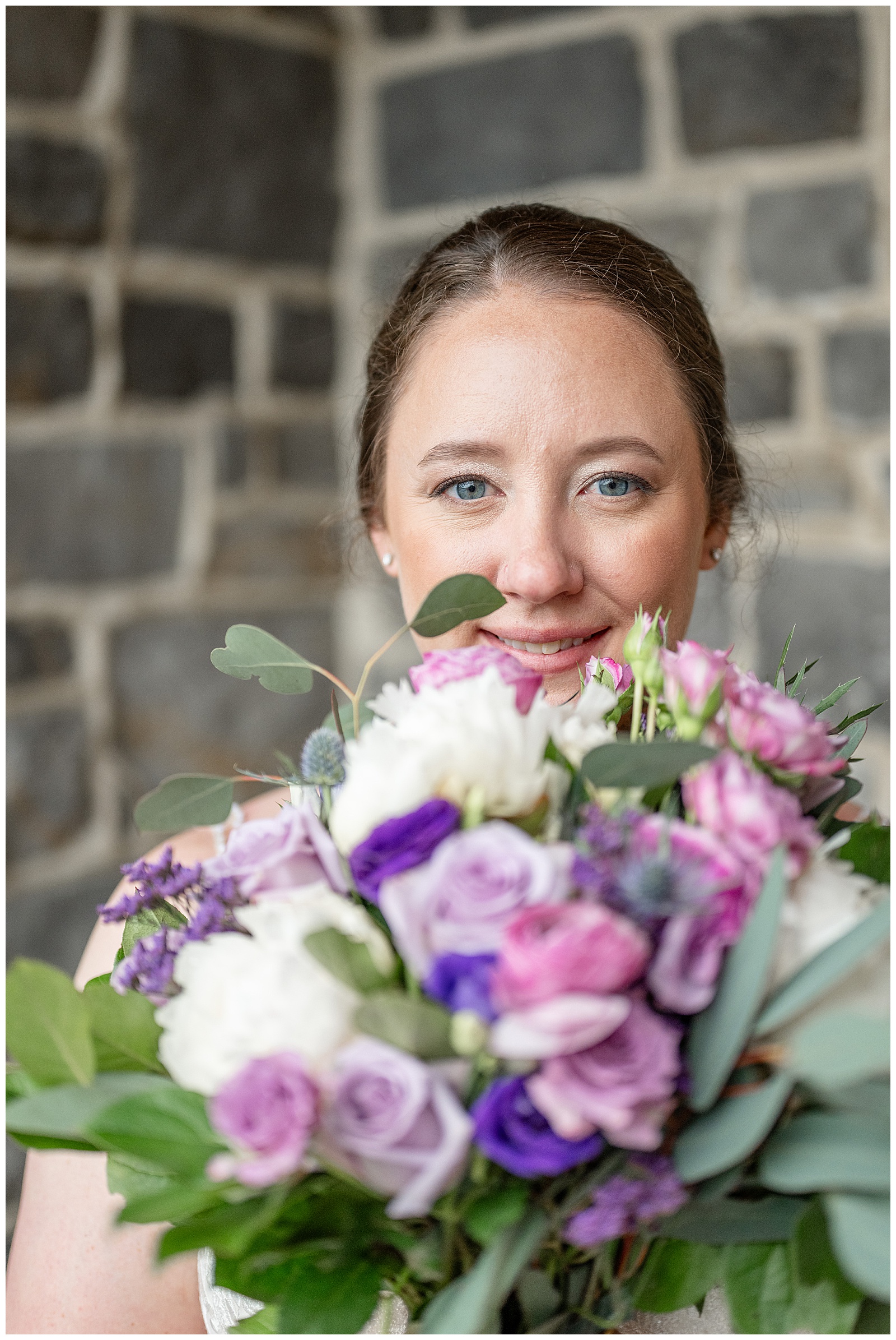 closeup photo of bride's face behind her bouquet of flowers in shades of purple and white at brick gables