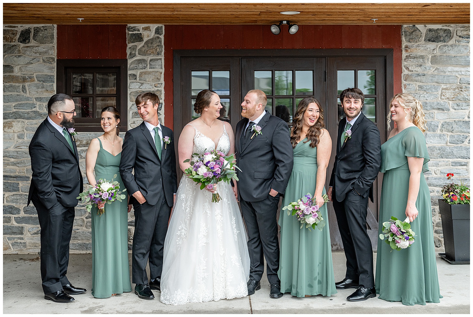 couple standing with their wedding party and everyone looking in different directions at brick gables on spring day