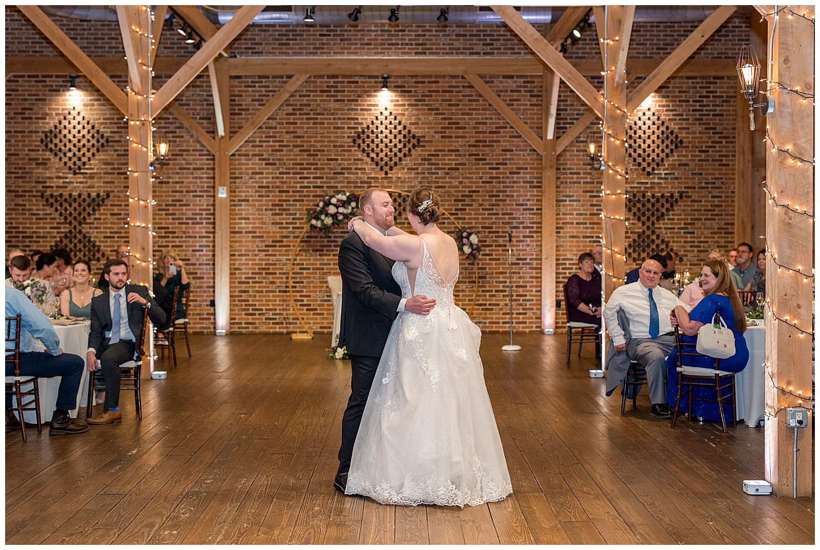 couple sharing their first dance during barn reception at brick gables as guests watch