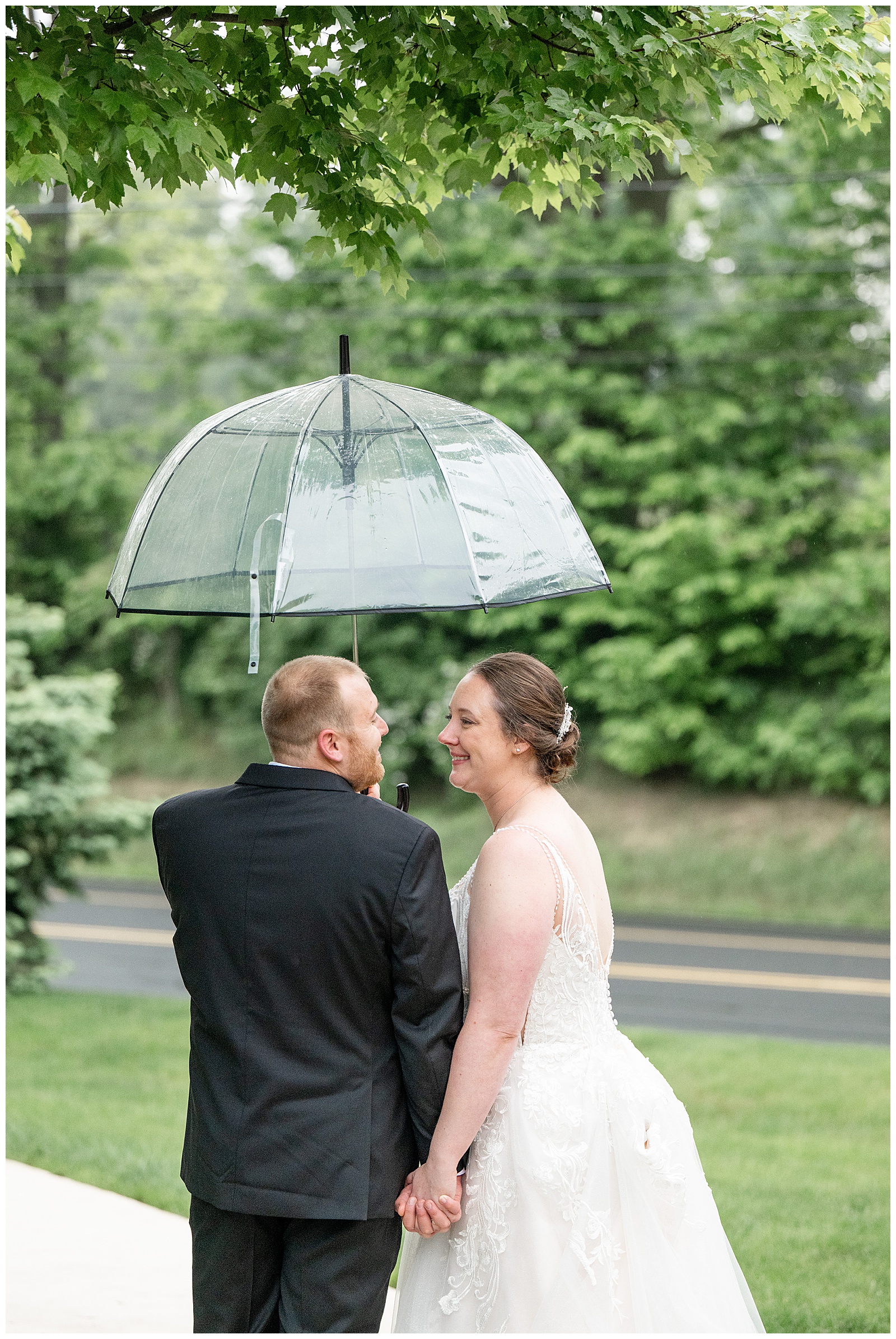 couple standing close under clear umbrella with backs toward camera on rainy day in lititz pa