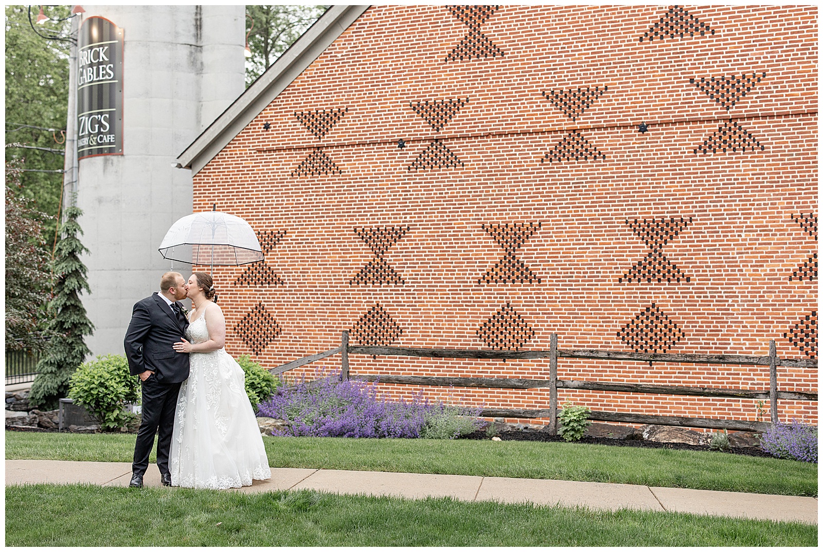 couple kissing under clear umbrella on sidewalk by brick barn at brick gables