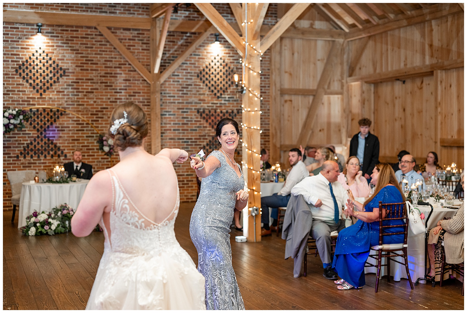 bride dancing with her mom as guests smile and watch at barn reception at brick gables