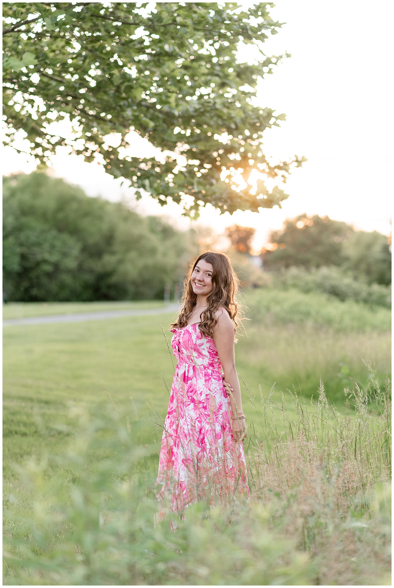 senior girl in pink and white dress by tall wild grasses at sunset at overlook park