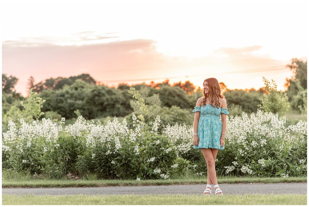 senior girl in blue and white off-the-shoulder dress looking to the right by white flowers at sunset in lancaster pa