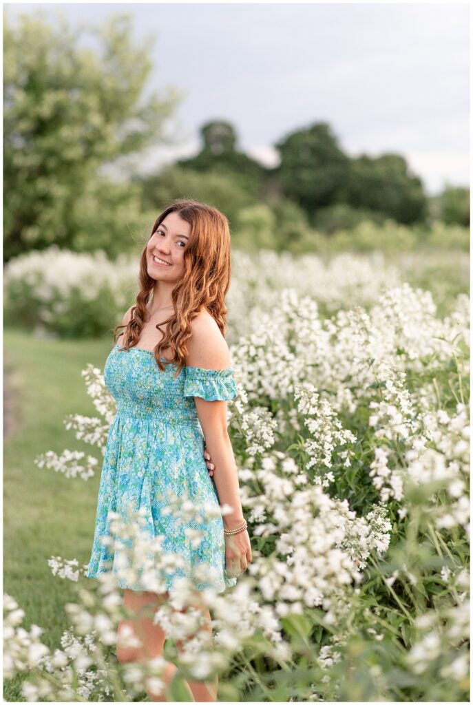 senior girl by tall white wildflowers with left shoulder toward camera at overlook park in lancaster county