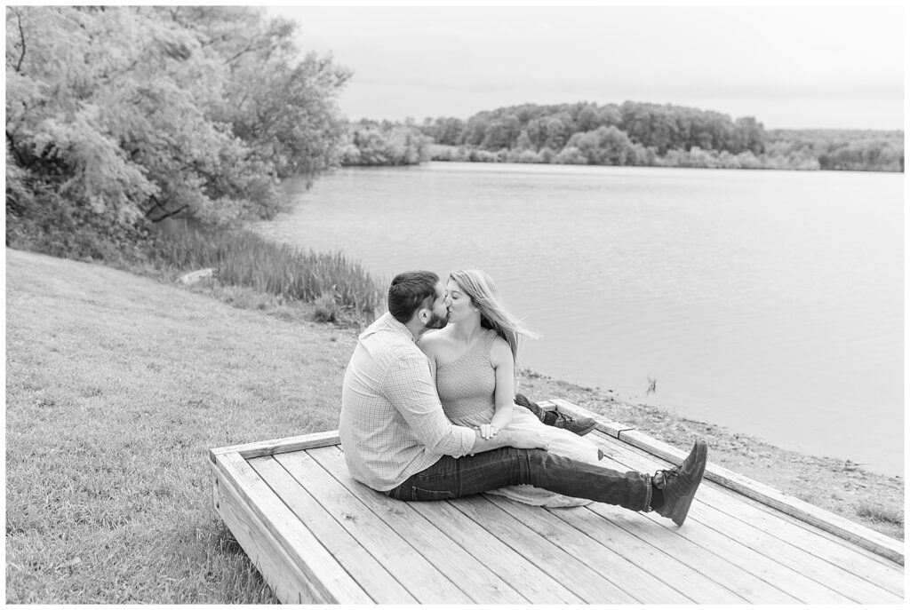 black and white photo of couple sitting on wooden dock by pond kissing at hibernia park