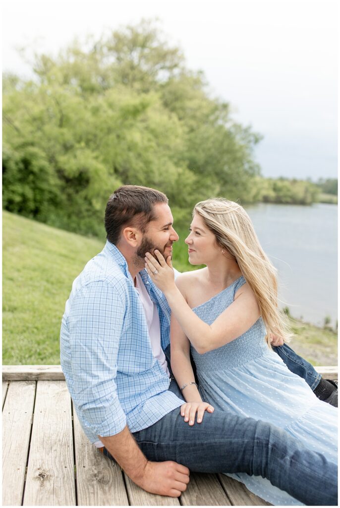 engaged couple sitting close and looking at each other as woman gently rests her left hand on man's jawline at hibernia park