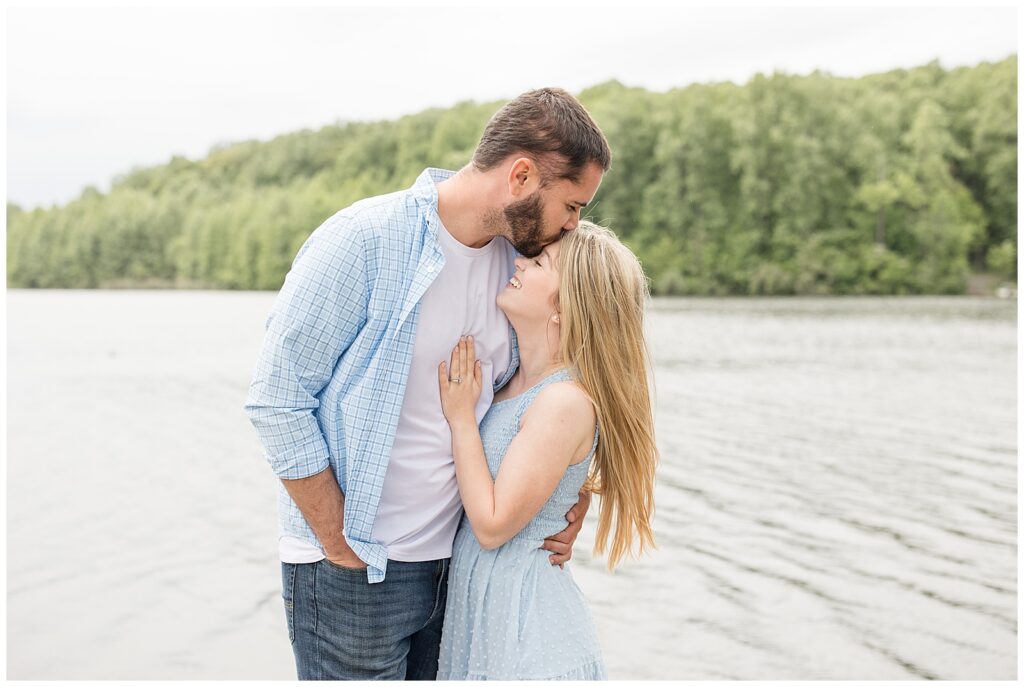 engaged couple hugging as man kisses his bride-to-be's forehead by pond at hibernia park