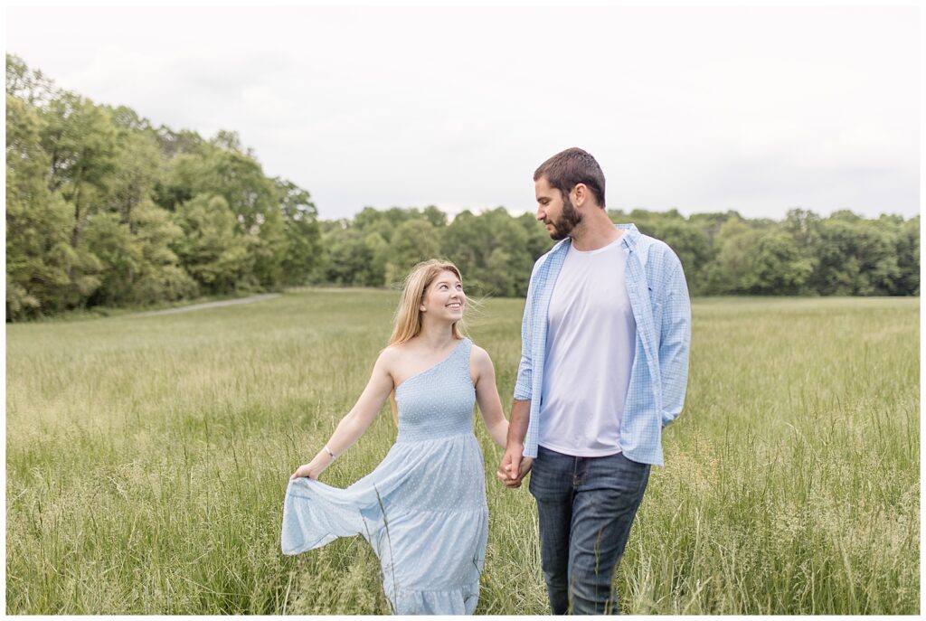 engaged couple holding hands and walking field of tall grasses at hibernia park in chester county