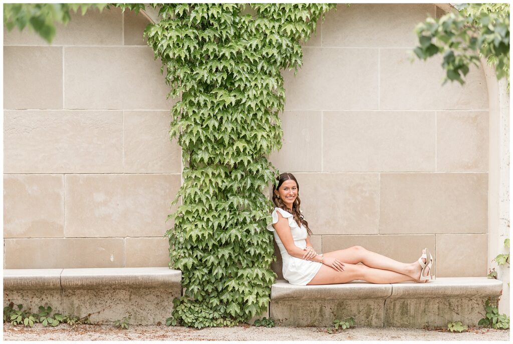 senior spokesmodel sitting with legs extended out on concrete bench by ivy archway in longwood gardens