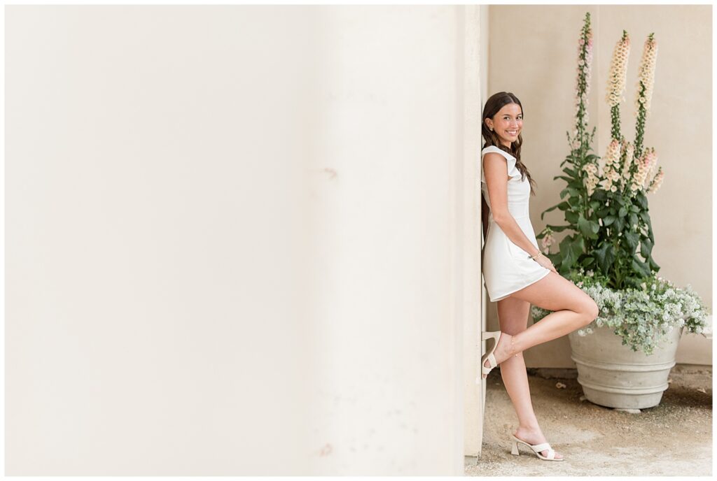 senior girl leaning against concrete wall with right foot propped against wall at longwood gardens in chester county pa