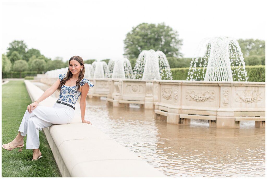 senior girl sitting along concrete wall by fountain at longwood gardens in kennett square pennsylvania