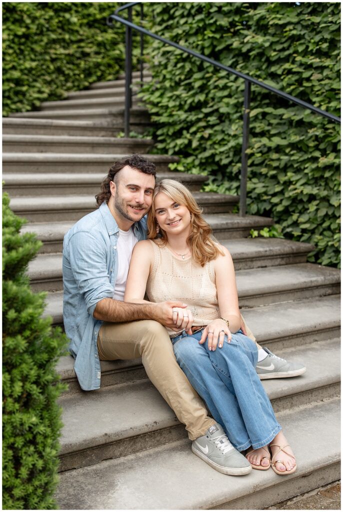 engaged couple sitting on concrete steps smiling at camera at longwood gardens