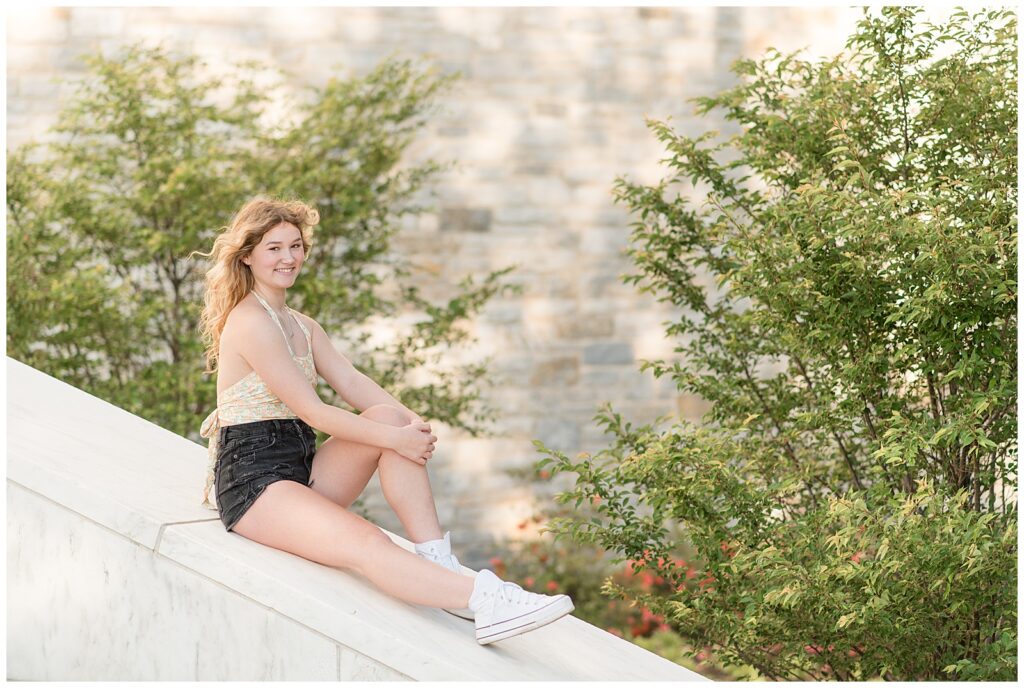 senior girl in pale tank top and black shorts sitting on angled ledge at founders hall in central pa