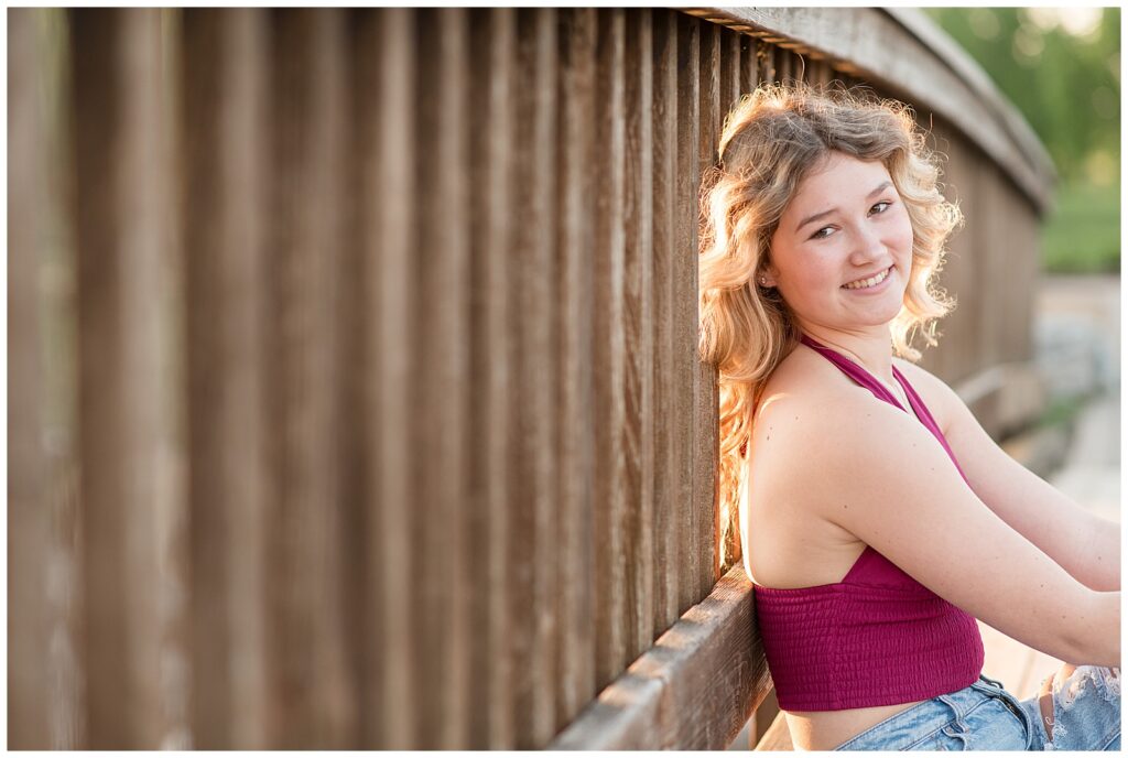 senior girl leaning back against slats of wooden bridge at sunset on spring evening at founders hall