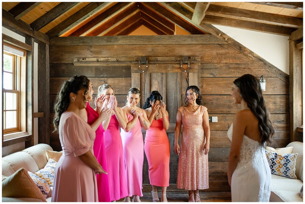 bridesmaids wearing different shades of bright pink dresses seeing bride in her gown at bridal suite