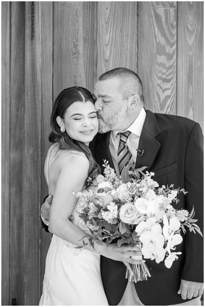 black and white photo of bride's father kissing her on her left cheek at domain pterion