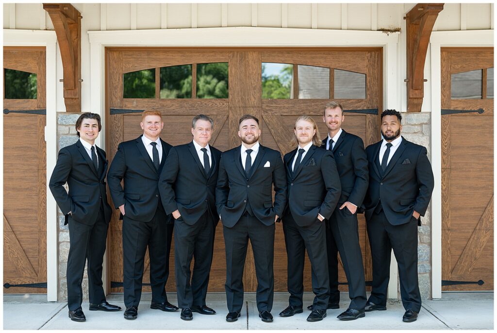 groom with his six groomsmen all wearing black suits and ties with their hands in their pockets