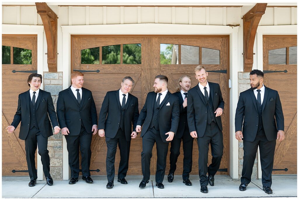 groom and groomsmen walking towards camera by brown garage door at domain pterion