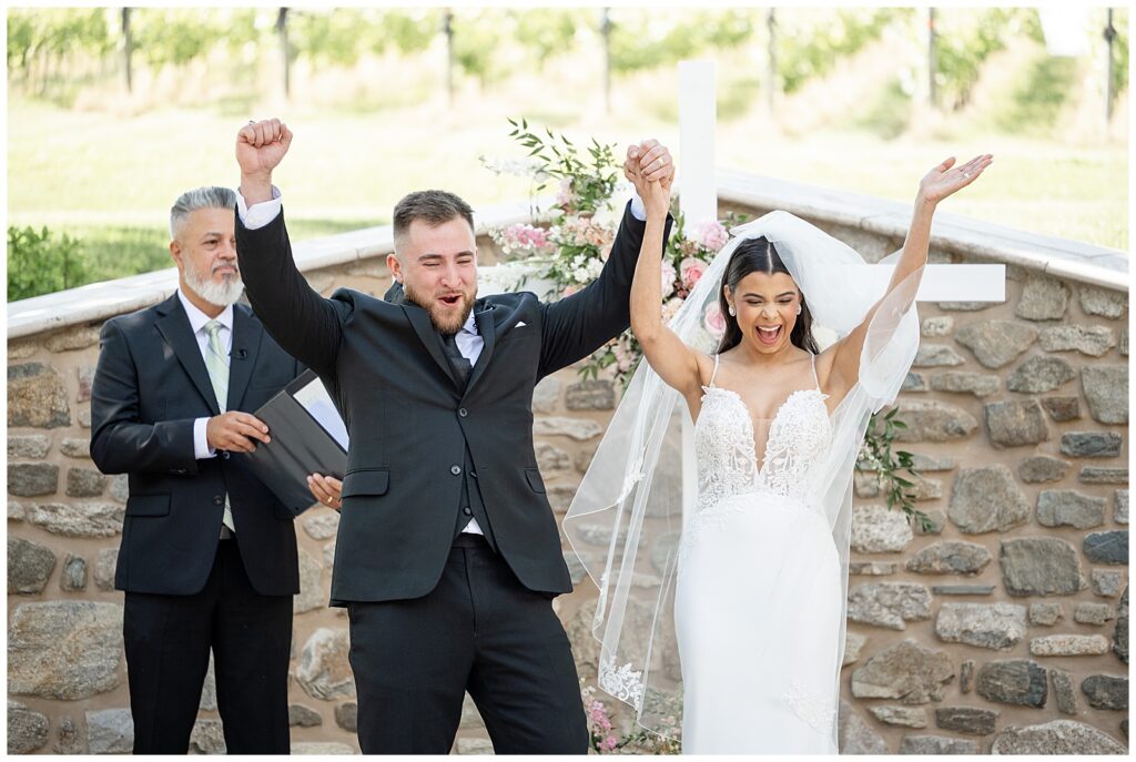 bride and groom holding hands and raising them high as they cheer and leave their wedding ceremony at domaine pterion