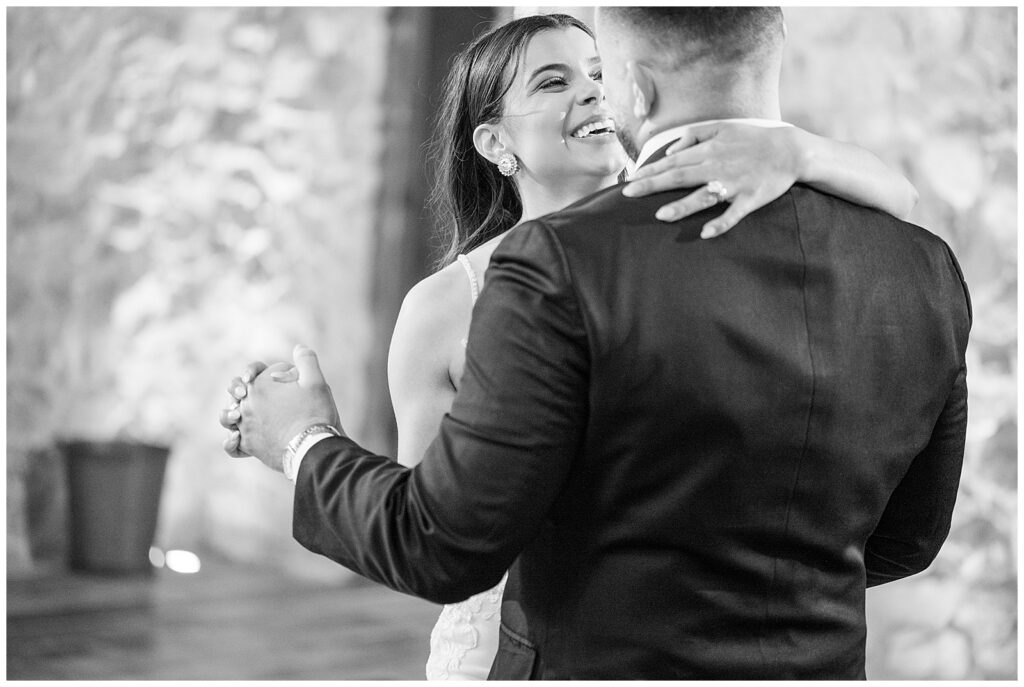 black and white photo of couple slow dancing with grooms back to camera and bride smiling at him