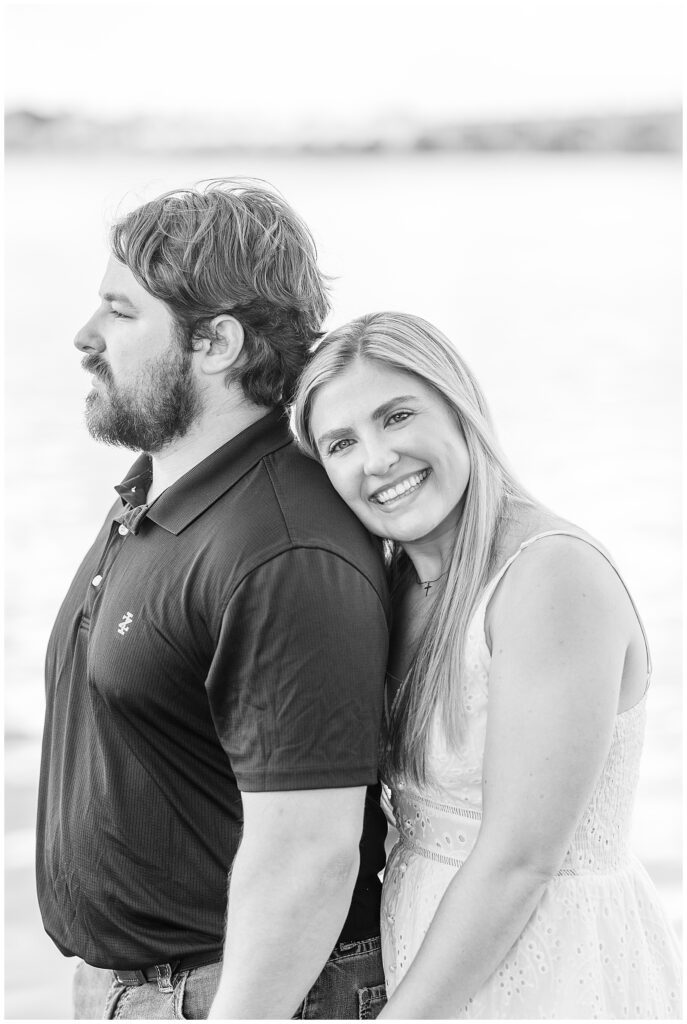 black and white photo of woman hugging her man from behind as she smiles at camera by susquehanna river