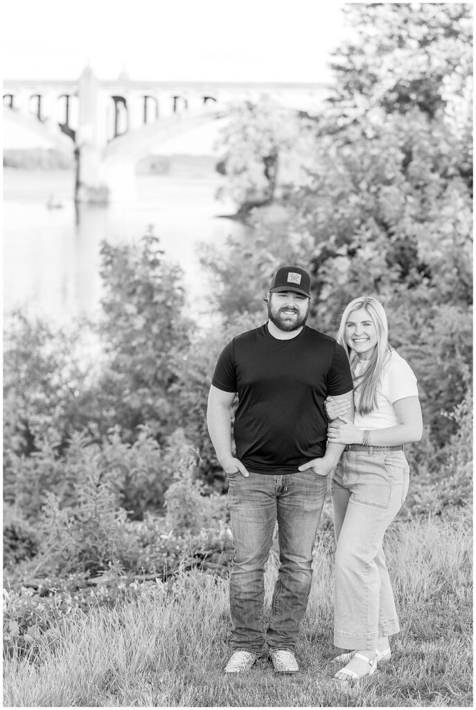 black and white photo of engaged couple smiling at camera by susquehanna river