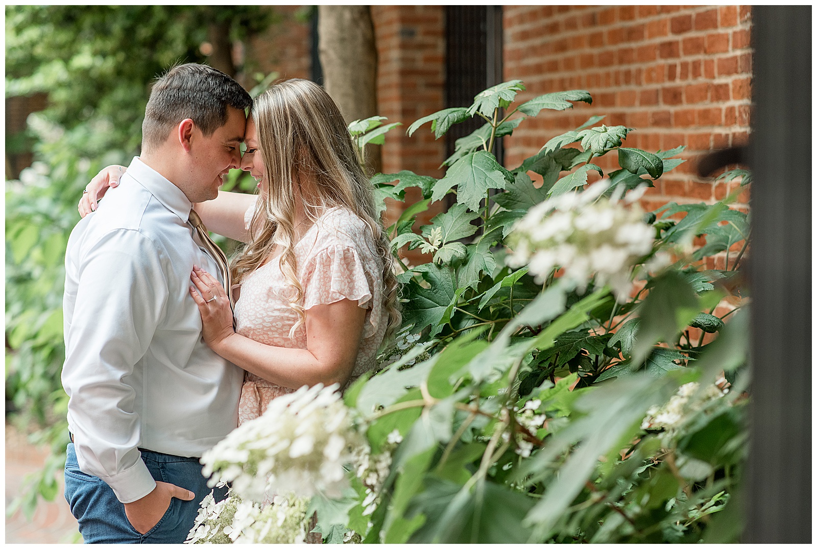 engaged couple touching their foreheads together by plants and brick wall at steinman park in lancaster pennsylvania