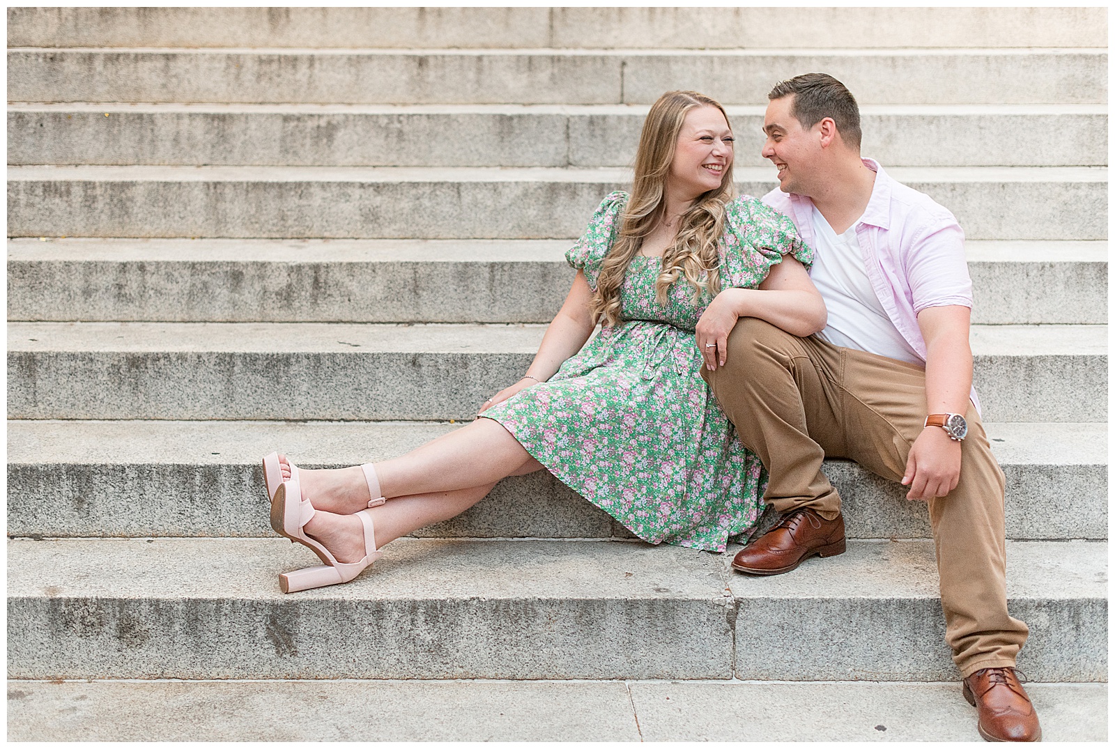 engaged couple sitting on concrete steps as they smile at each other in lancaster city