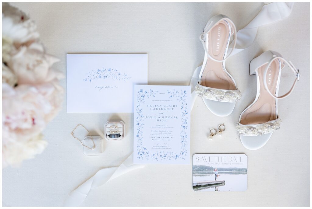 wedding details like ring boxes, invitation, bride's shoes, and more on display atop white table at ironspire complex