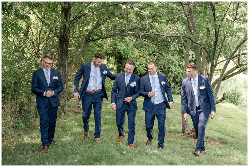 groom and groomsmen all walking towards camera in wooded lawn of ironspire complex in adamstown pennsylvania