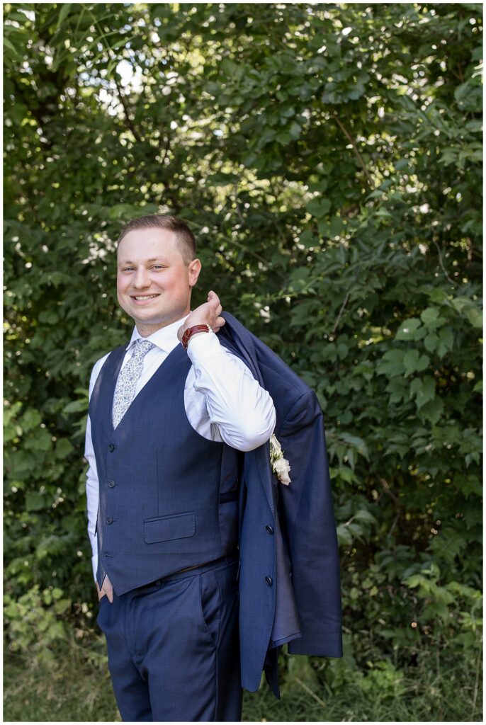 groom smiling at camera as he holds his suit coat over his left shoulder at ironspire complex