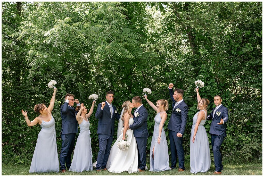 bridal party cheering for bride and groom as they kiss by wooded area at ironspire complex