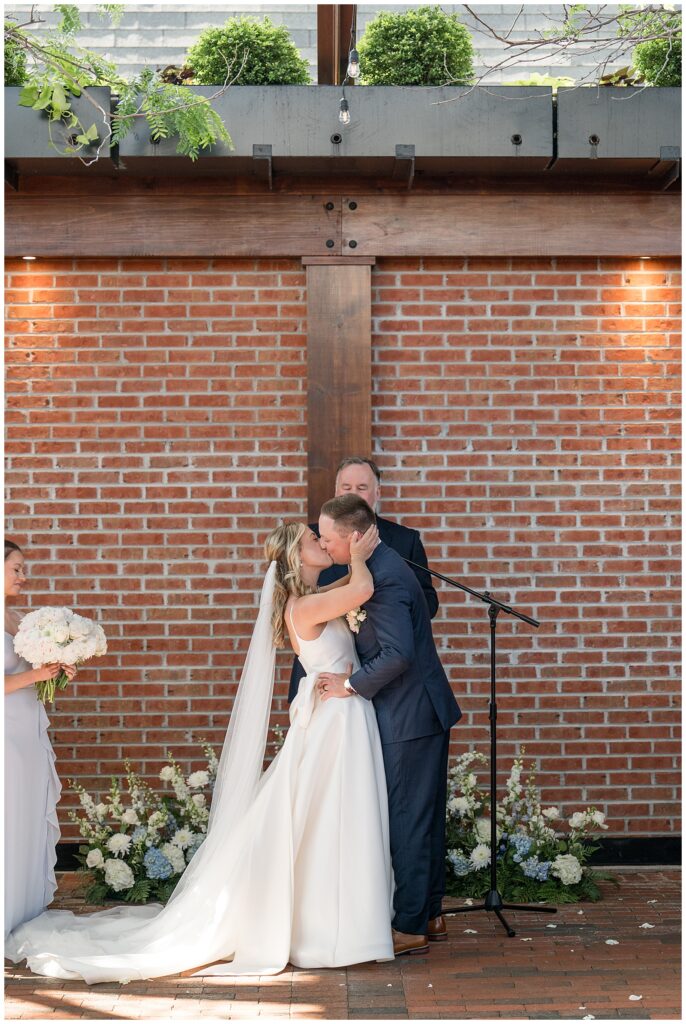 bride and groom share their first kiss by brick wall at ironspire complex in lancaster pennsylvania