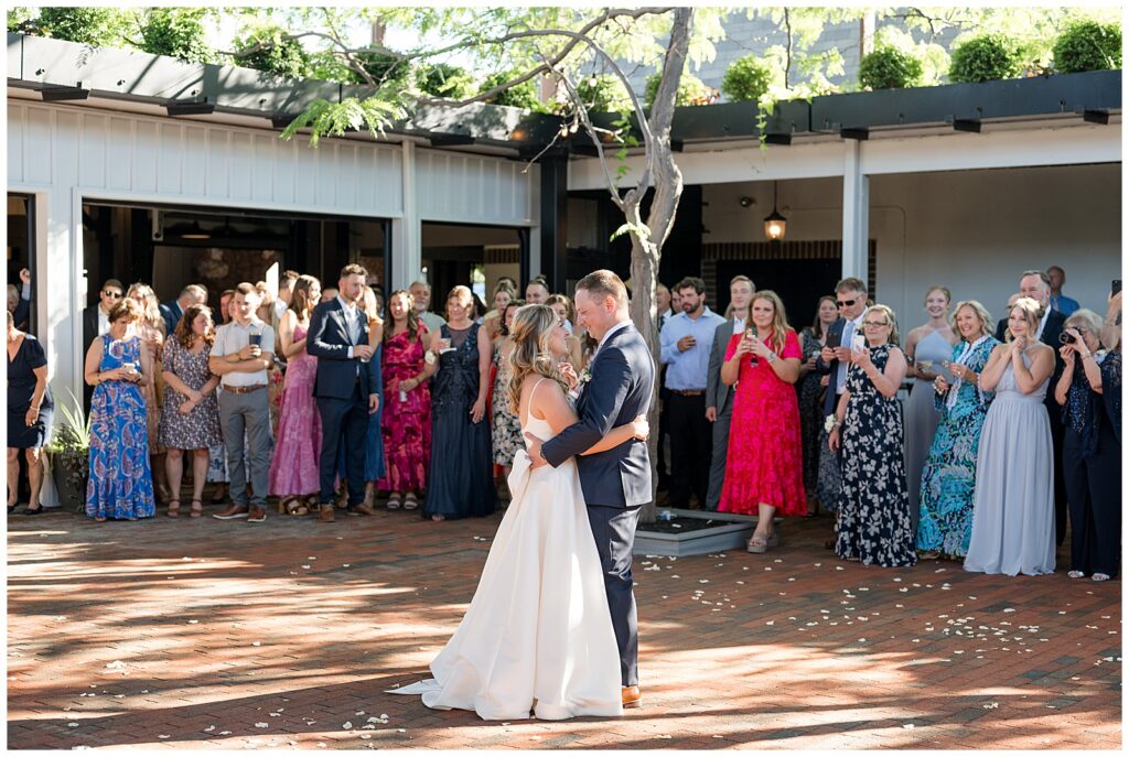 bride and groom share their first dance outdoors in courtyard surrounded by wedding guests on sunny June day at ironspire complex